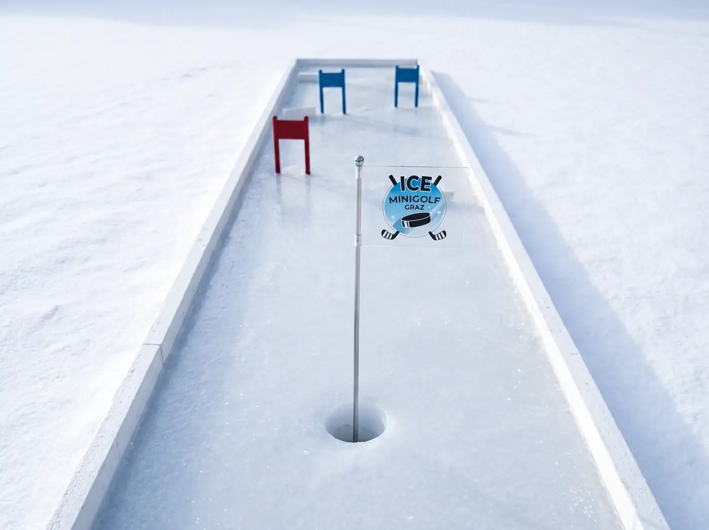 Vorschau einer geraden Eisbahn im Schnee mit blauen und roten Hindernissen, Loch und Fähnchen mit dem Ice-Minigolf-Logo.